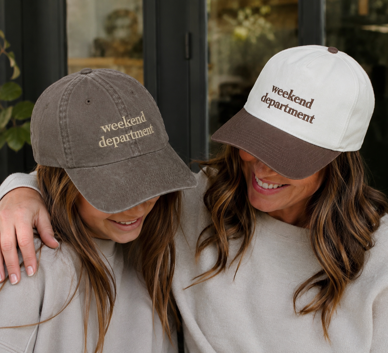A woman and a child wearing matching baseball caps with the words 'weekend department' embroidered on the front. The woman wears a natural cap with a brown brim, and the child wears a brown washed cap.