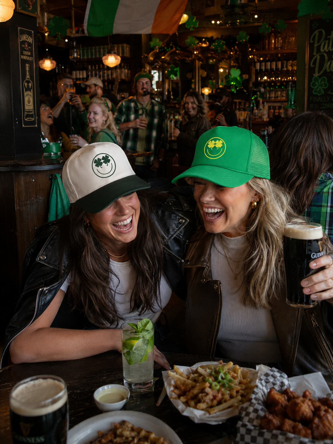 Two women laughing at a St. Patrick's Day pub, wearing green and white trucker hats
