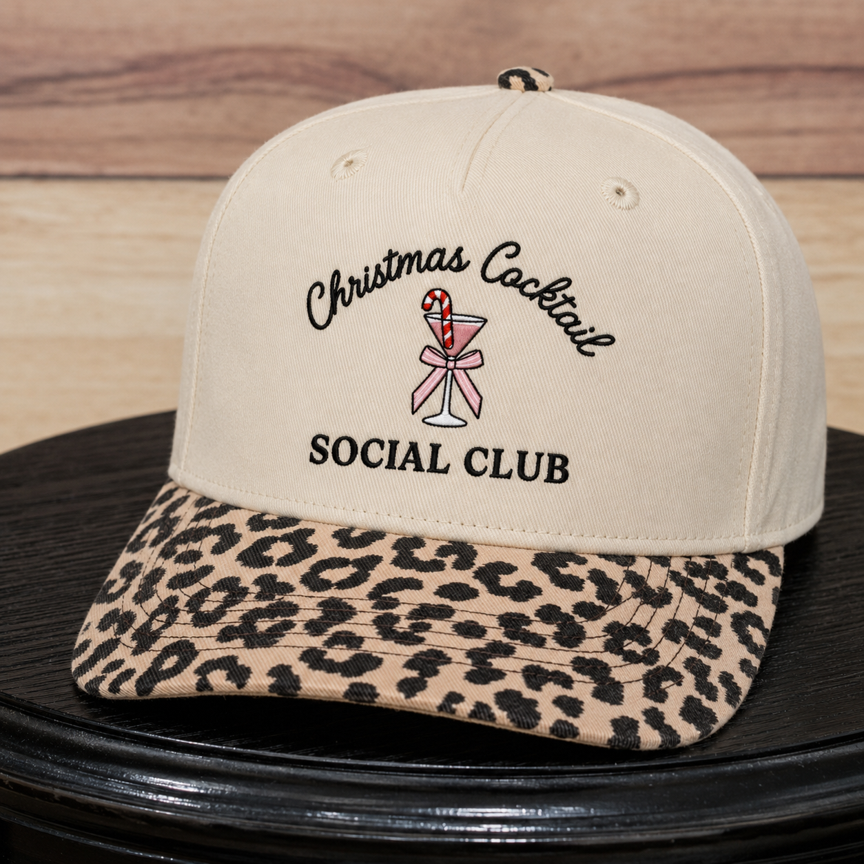 A beige baseball cap with a leopard-print brim, featuring embroidered text that reads 'Christmas Cocktail SOCIAL CLUB' with a cocktail glass and candy cane graphic on the front.